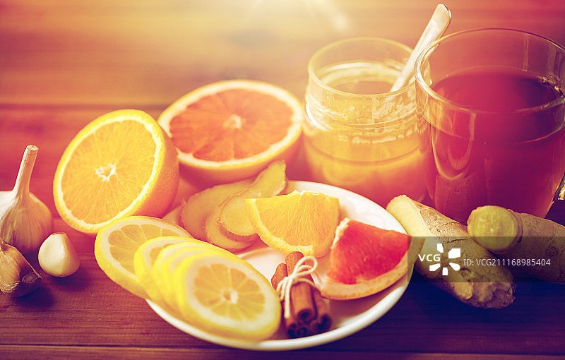 健康，传统医学，民间疗法和民族科学概念-一杯姜茶与蜂蜜，柑橘和大蒜在木制背景。姜茶加蜂蜜，柑橘和大蒜在木头上图片素材