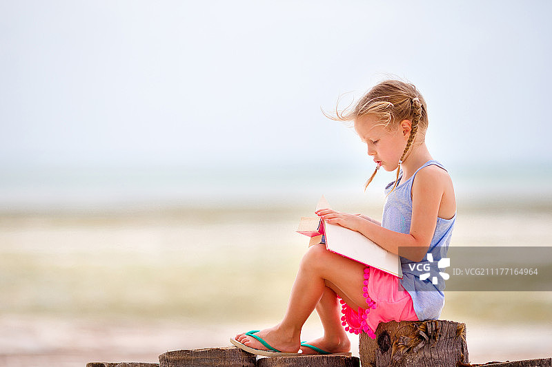 可爱的小女孩在热带的白色沙滩上看书图片素材