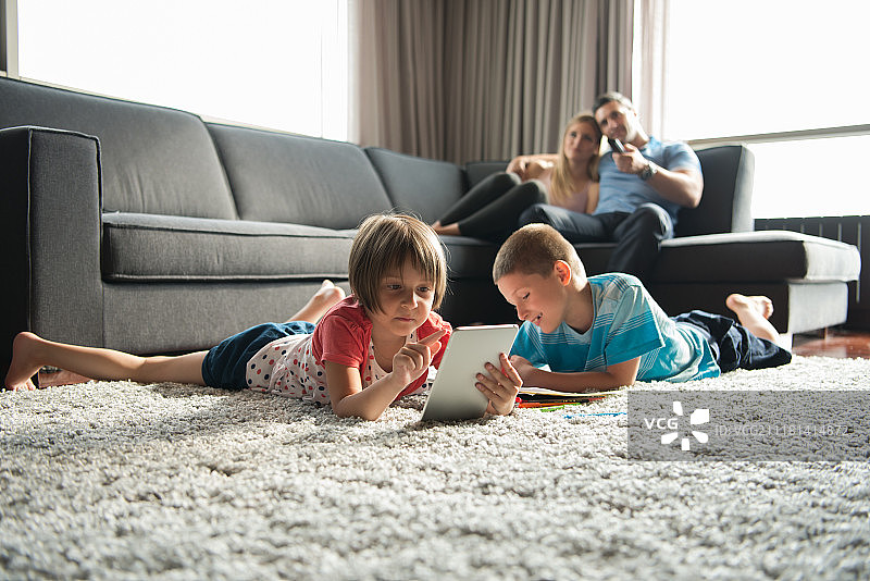 快乐的年轻家庭一起玩在家里的地板上使用平板电脑和儿童绘画集图片素材