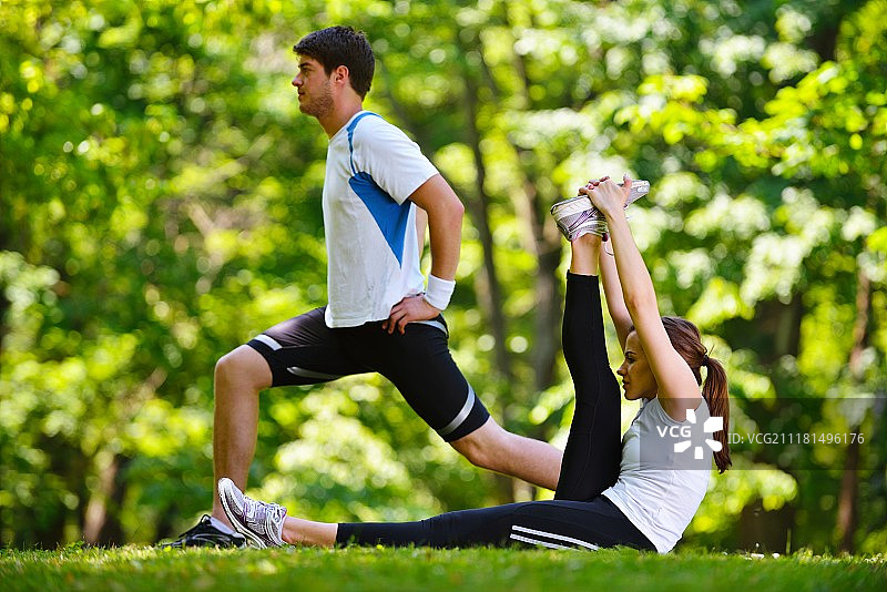 一对健康的年轻夫妇在公园慢跑和跑步后做伸展运动，放松和热身图片素材