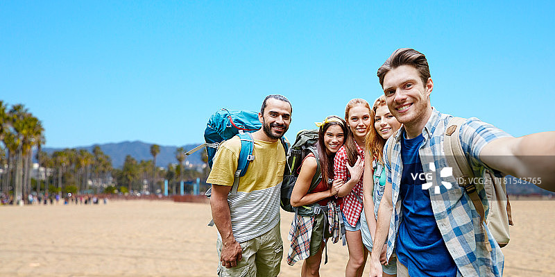 科技，旅游，旅游，徒步和人的概念-一组微笑的朋友与背包自拍大海岸的加利福尼亚背景。背包朋友在自拍。背包朋友在自拍图片素材
