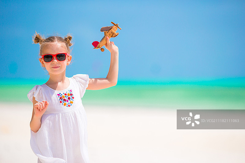可爱的小女孩与玩具飞机在白色的海滩图片素材