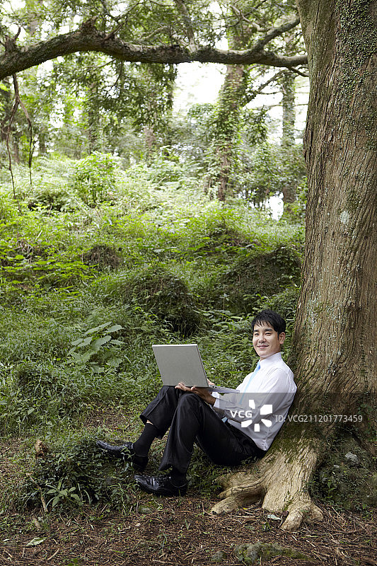 商人坐在树上用笔记本电脑在森林里工作的照片图片素材