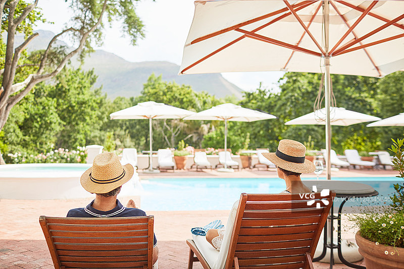 一对夫妇在阳光明媚的度假村泳池边的躺椅上放松图片素材