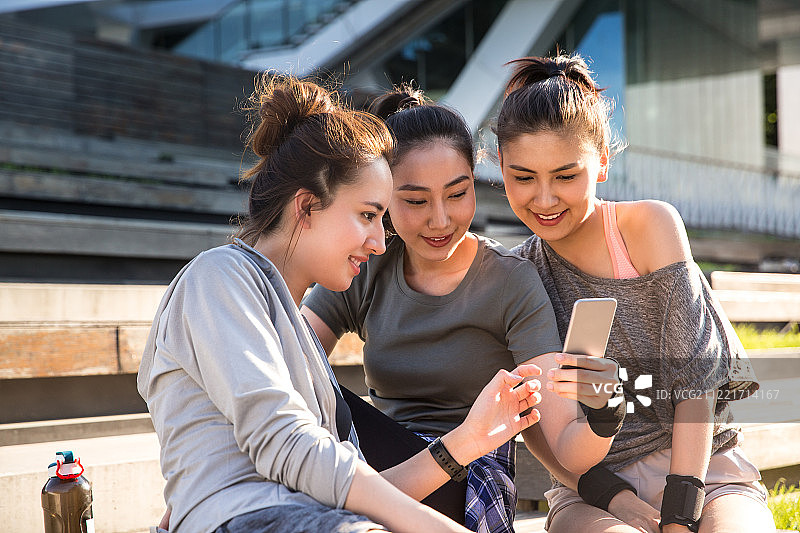 三个青年女子在户外运动后坐在地上休息玩手机图片素材