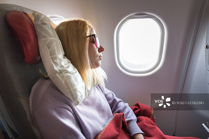 疲倦的金发休闲白种人女士在座位上睡觉，而旅行乘飞机。商业……图片素材