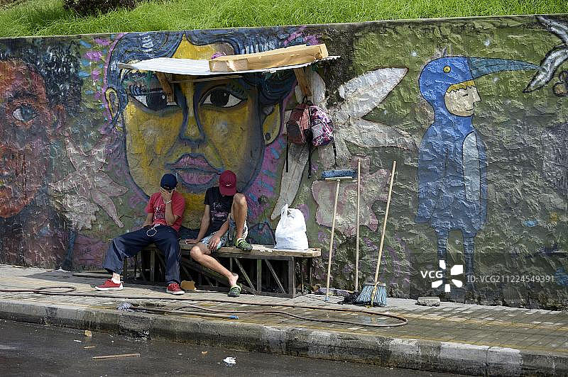 南美哥伦比亚，安提奥基亚省，麦德林，Comuna 8贫民窟，年轻的帮派成员坐在涂鸦墙前图片素材