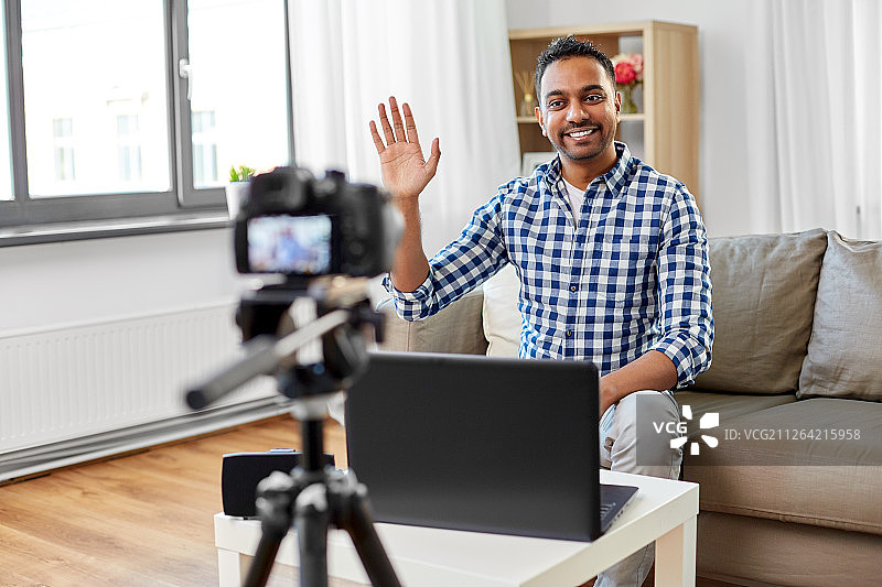 博客，视频博客和人的概念-微笑的印度男性博客用相机记录视频，并在家里办公室挥手。男性博客在家里用摄像机拍摄视频图片素材