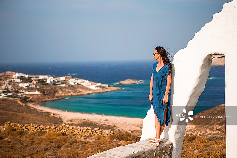 身穿蓝色裙子的中年妇女，旁边是以海湾为背景的白色拱门图片素材