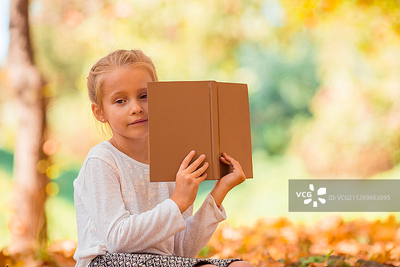 秋天，女孩坐在棕色的树叶上看书图片素材
