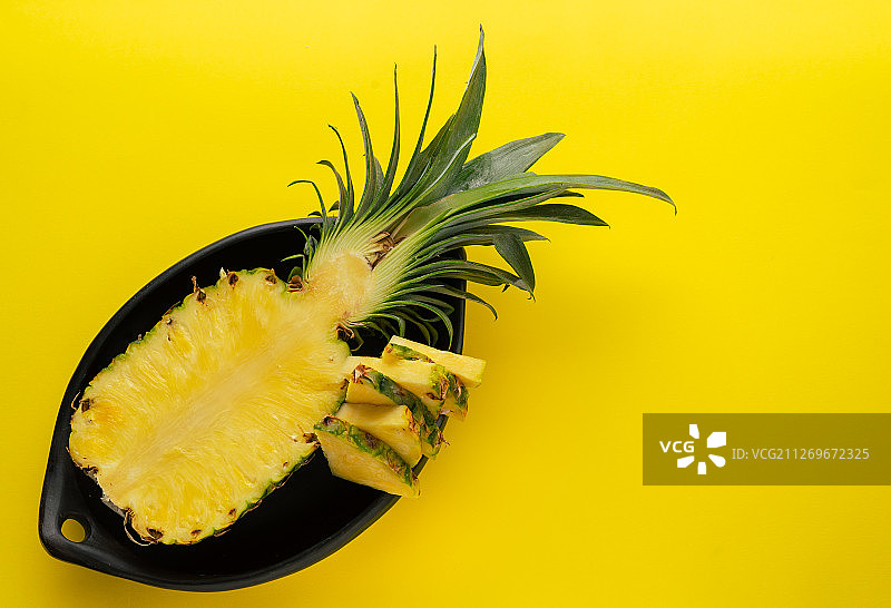 将菠萝切于黑色碗中，背景为黄色。图片素材