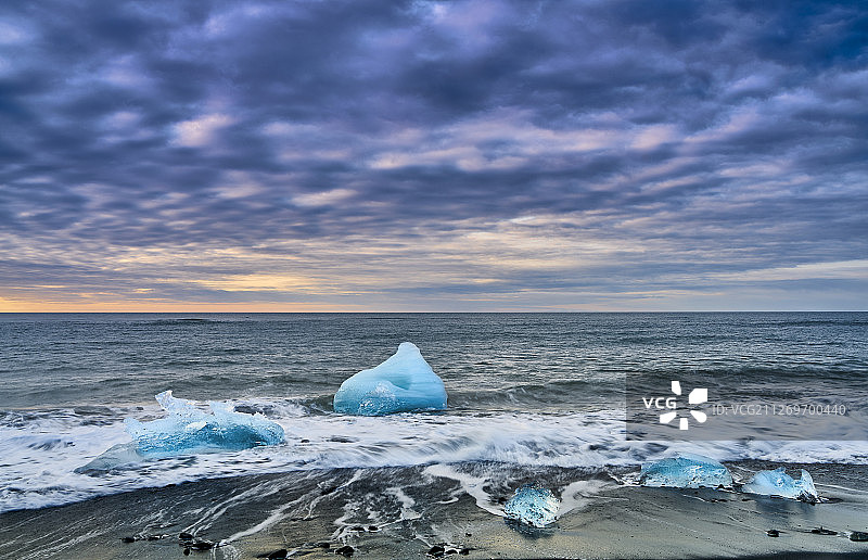 荧光蓝色的冰块被海浪冲刷到海岸上图片素材