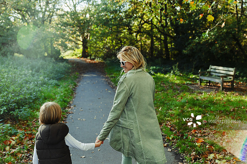 快乐的母子手牵着手漫步在阳光明媚的秋日公园里图片素材