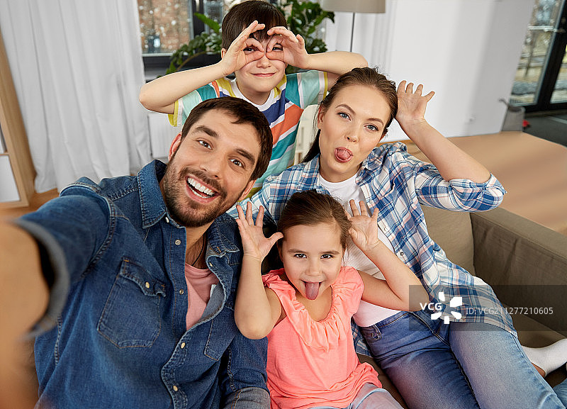 家庭，乐趣和人的概念-快乐的父亲，母亲，小儿子和女儿在家里自拍和做鬼脸。家人在家里自拍和做鬼脸图片素材