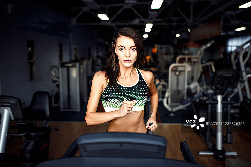 年轻的健身女性在健身房做有氧运动，在跑步机上跑步图片素材