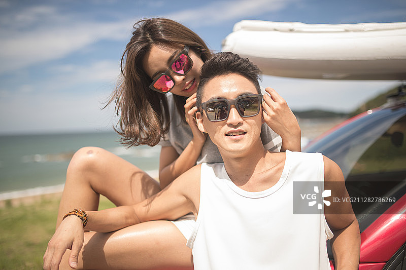 一对夫妇戴着太阳镜倚靠在停在海滩上的汽车上的照片图片素材