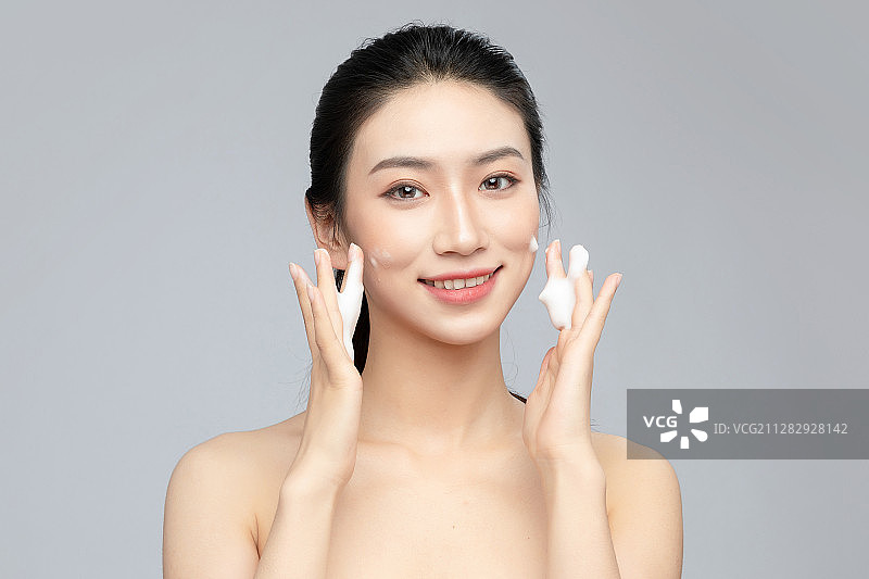 灰色背景里正在使用洗面奶的亚洲美女面部特写，化妆护肤整容图片素材