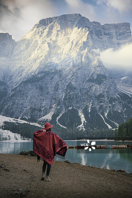 意大利特伦蒂诺-上阿迪杰，南蒂洛尔布雷斯，一名身穿传统红色斗篷和帽子的妇女，正在欣赏山和湖的景色图片素材
