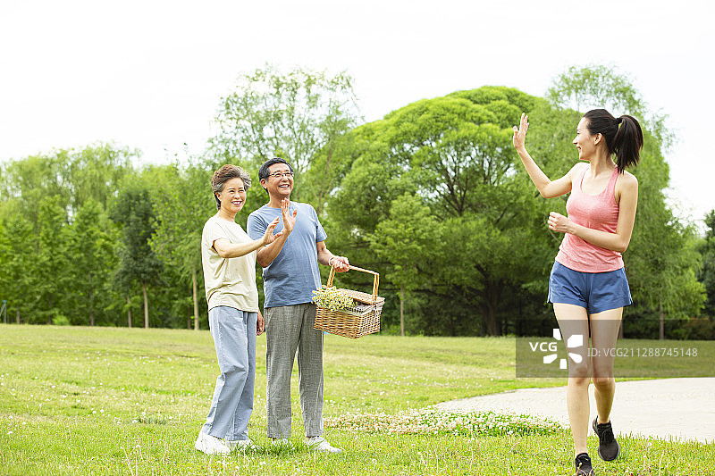 青年女子帮助老年夫妻拿野餐篮子后挥手告别在户外公园图片素材