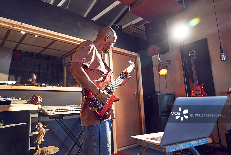 男音乐家在录音室的笔记本电脑练习吉他图片素材