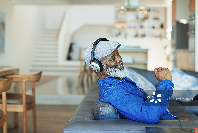 快乐的男人戴着耳机在客厅的沙发上听音乐图片素材