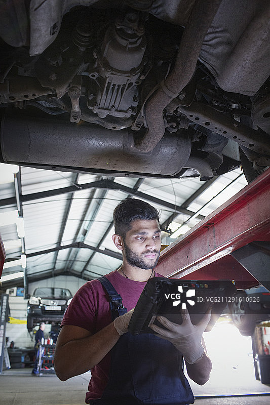 男机械师在汽车修理厂使用汽车下的诊断设备图片素材