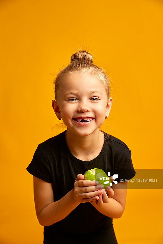 小女孩(6-7岁)穿着黑色休闲衬衫，拿着苹果微笑，露出掉了的乳牙图片素材