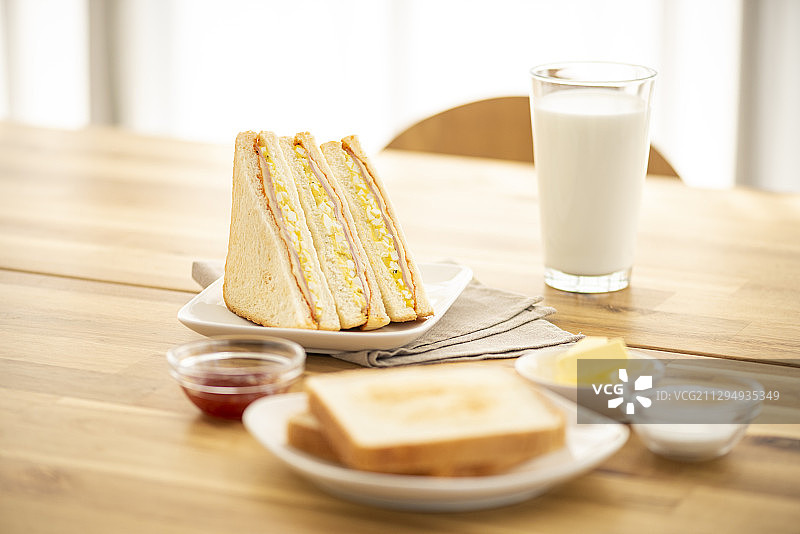 三明治和面包片放在盘子里，黄油和酱汁放在一杯牛奶旁边图片素材