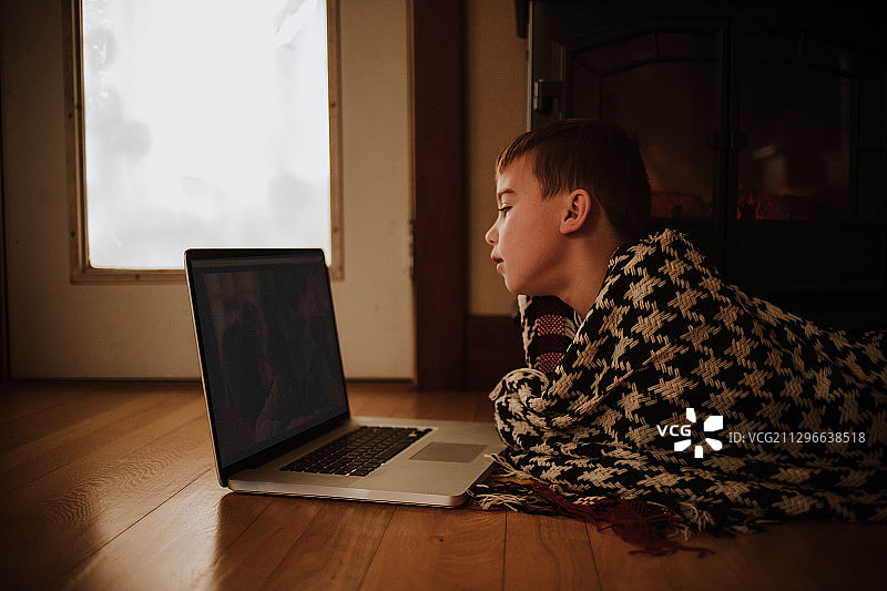 男孩躺在家里地板上用笔记本电脑看电影的侧视图图片素材