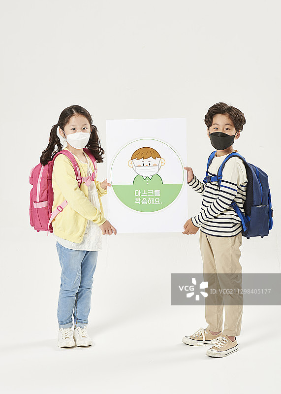 小学男孩和女孩戴着污染口罩站着，手持安全规则的信息图片素材