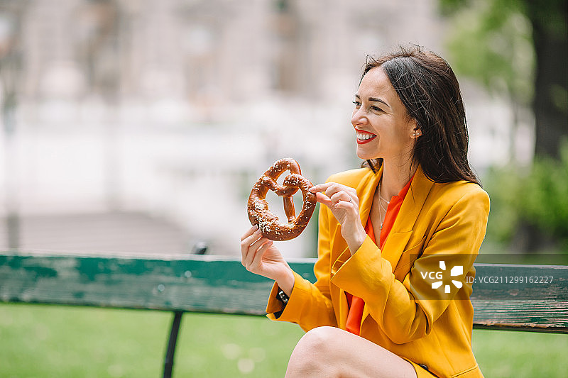 美丽的女人拿着椒盐卷饼，在公园里放松图片素材