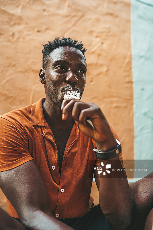 年轻英俊的黑人男子穿着橙色衬衫吃冰淇淋，科帕颜，泰国图片素材