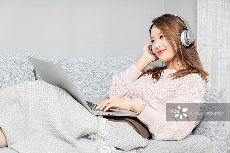 躺在沙发上带着耳机使用电脑亚洲女孩图片素材