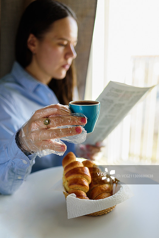 戴着防护手套在咖啡店吃早餐的女人图片素材
