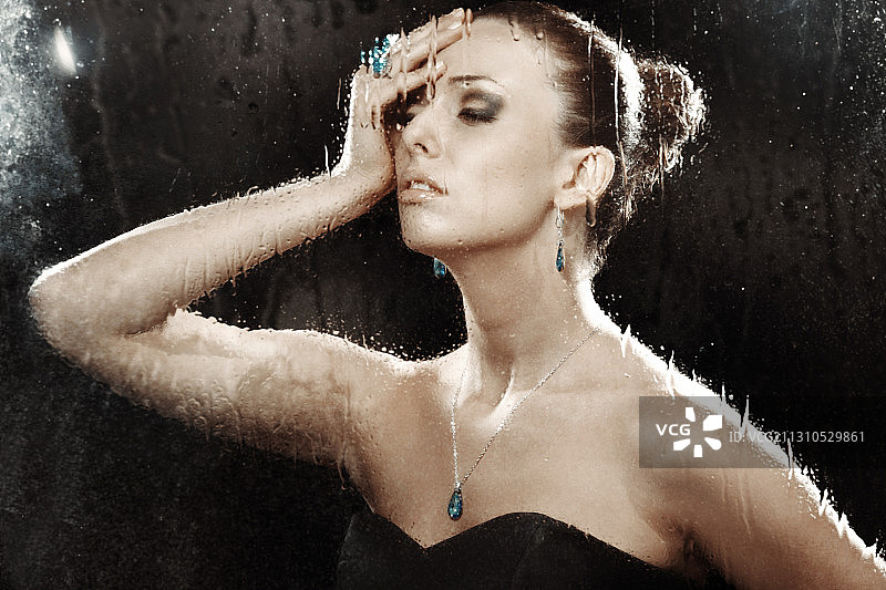 戴着珠宝的女人躲在湿玻璃后面图片素材