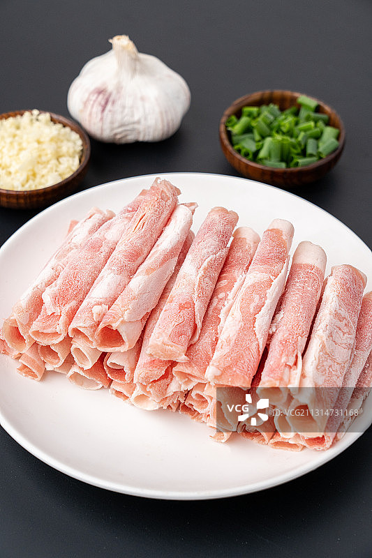 低调灰色厚重背景大理石上盘子里的成排美食羊肉卷及火锅蔬菜配菜图片素材