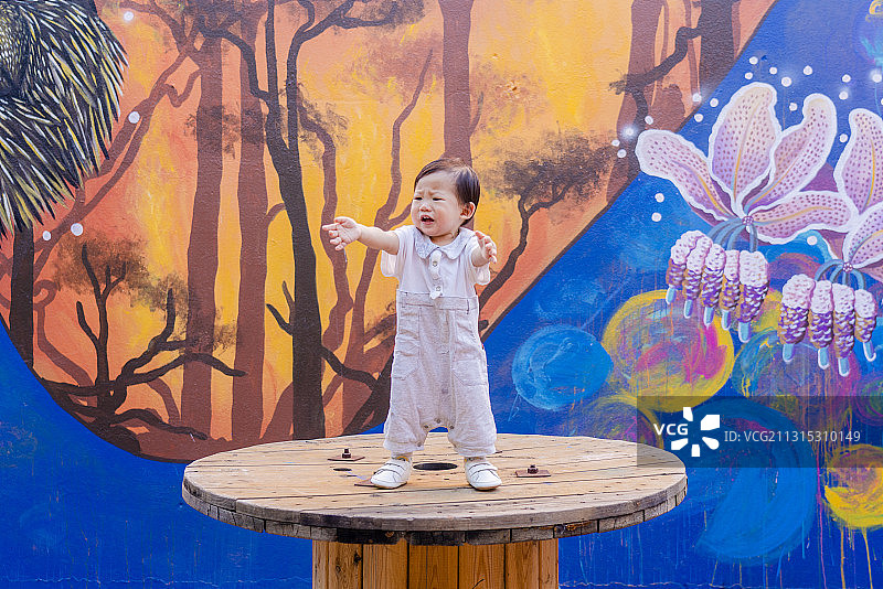 勇敢地站在艺术墙前的木盘上的男婴图片素材