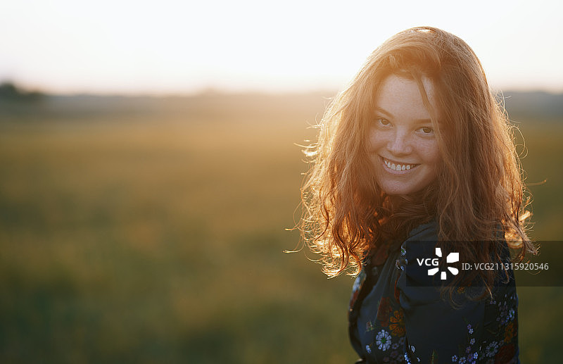美丽的红发年轻女子享受草地在日落图片素材