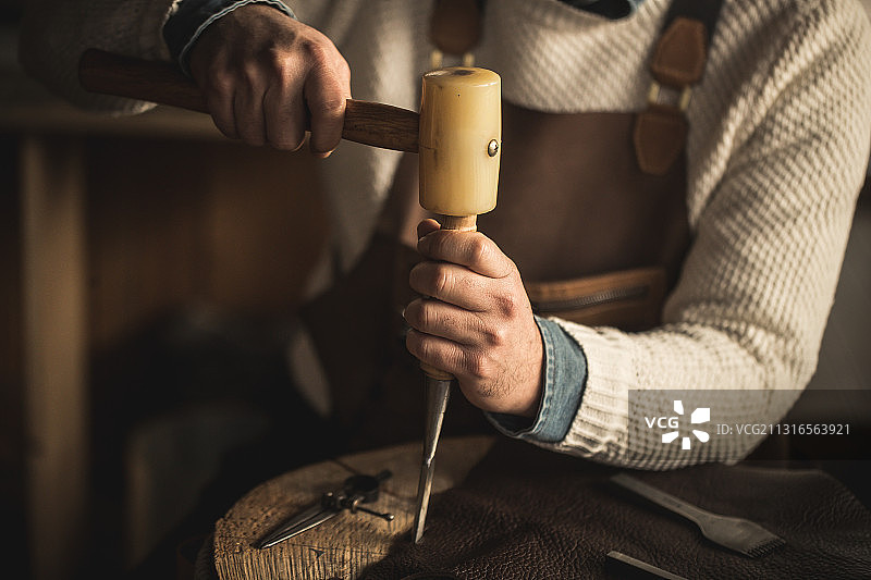 特写的成熟男子工作皮革工艺与锤在车间图片素材