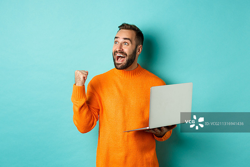 一个微笑的男人拿着笔记本电脑，站在蓝色背景下图片素材