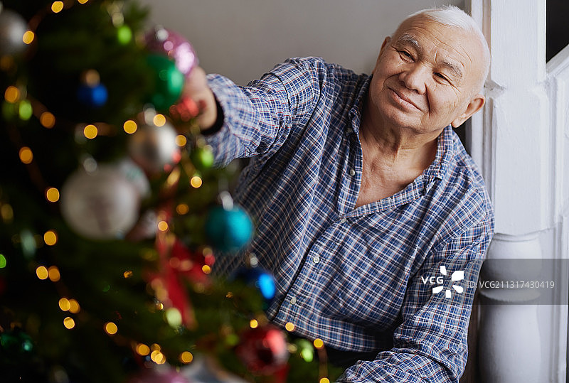 在装饰过的圣诞树旁，一位安详的老人的肖像图片素材