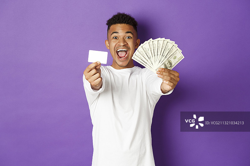 在紫色背景下，一个微笑的年轻人拿着纸币的肖像图片素材