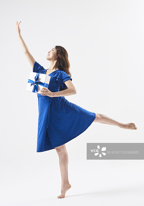 穿着蓝色连衣裙的女子站在芭蕾舞动作拿着带蓝色丝带的礼盒图片素材