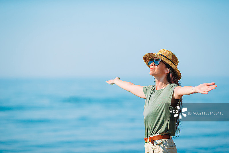 在天空的映衬下，女人张开双臂站在海滩上图片素材