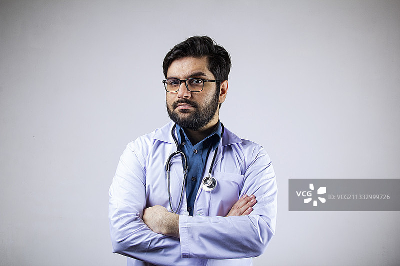 一个自信的医生双手交叉站在灰色背景下的肖像图片素材