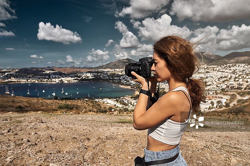 一名女子站在陆地上，对着天空拍照的侧视图图片素材