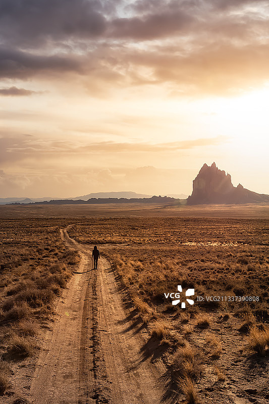 一个女人走在干燥的沙漠里的一条土路上图片素材
