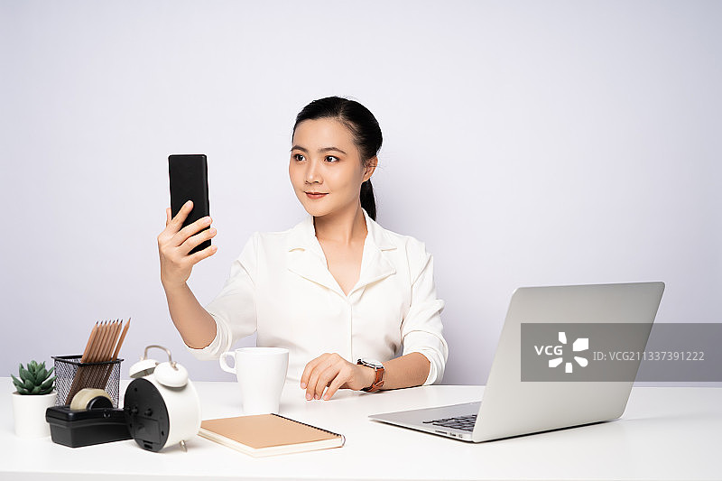 女商人坐在办公室的办公桌前使用手机的肖像图片素材