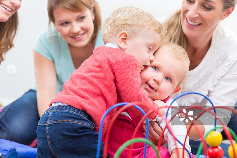 一群快乐的年轻母亲看着他们可爱和健康的婴儿，同时玩五颜六色的玩具在一个现代日托中心图片素材