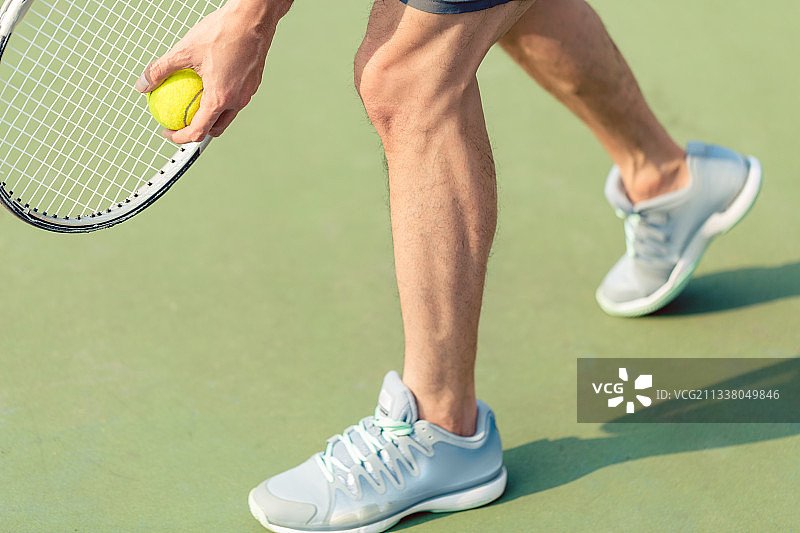 在绿色地面上比赛时，职业运动员穿着灰色运动鞋并拿着球和网球拍的低处图片素材